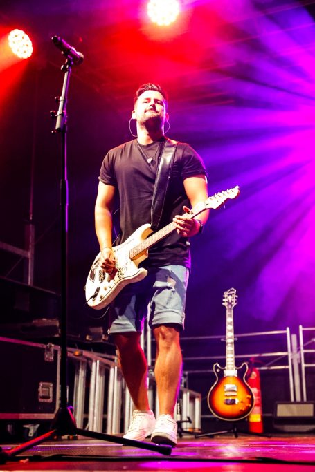Musiker auf der Bühne mit E-Gitarre und bunten Lichtern im Hintergrund.