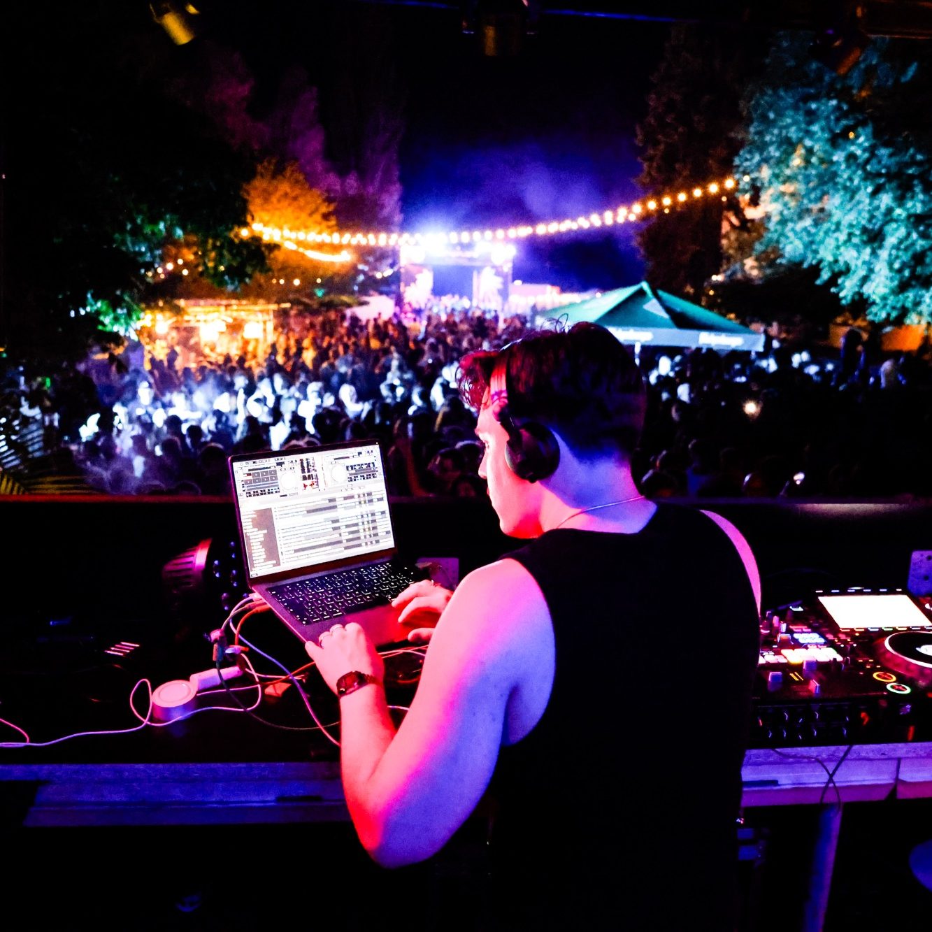 DJ steuert Musik vor einer großen Menschenmenge bei Nachtveranstaltung.