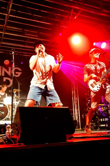 Männer in Jeans und T-Shirts treten auf einer Bühne mit bunten Lichtern auf.