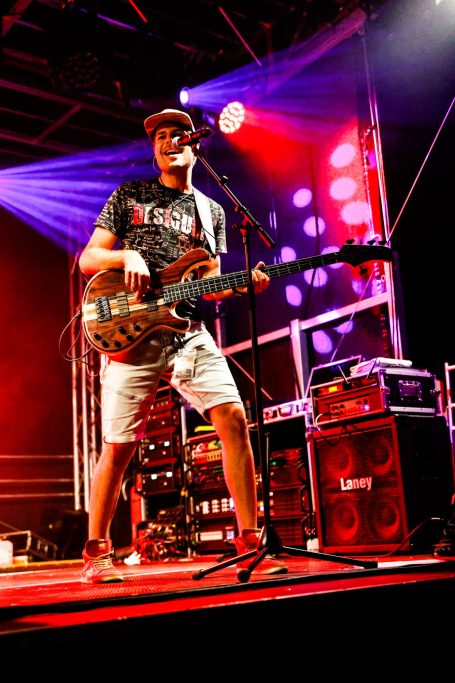 Musiker mit Gitarre auf der Bühne, umgeben von bunten Lichtern.