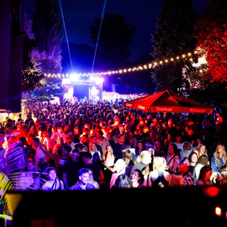 Menschenmenge bei einem nächtlichen Festival mit bunten Lichtern und Ständen.