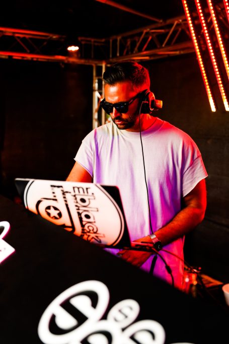 DJ am Mischpult mit Sonnenbrille, umgeben von bunten Lichtern.