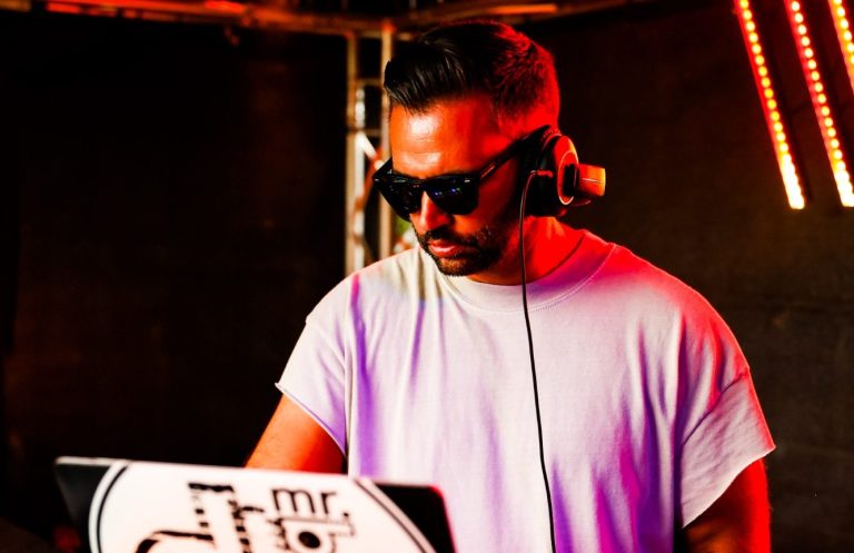 DJ Mr. Black Sumpfland Festival DJ Mr. Black mit Kopfhörern und Sonnenbrille an einem Mischpult mit bunten Lichtern.