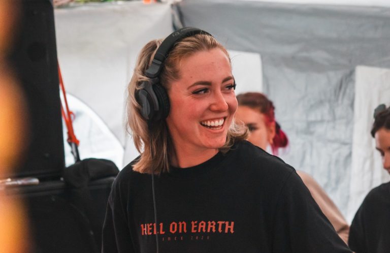 Lächelnde DJ mit Kopfhörern und schwarzem T-Shirt, fröhlich beim Auflegen.