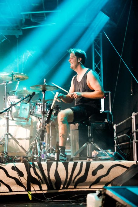 Ein Schlagzeuger spielt auf einer Bühne mit starker Beleuchtung.