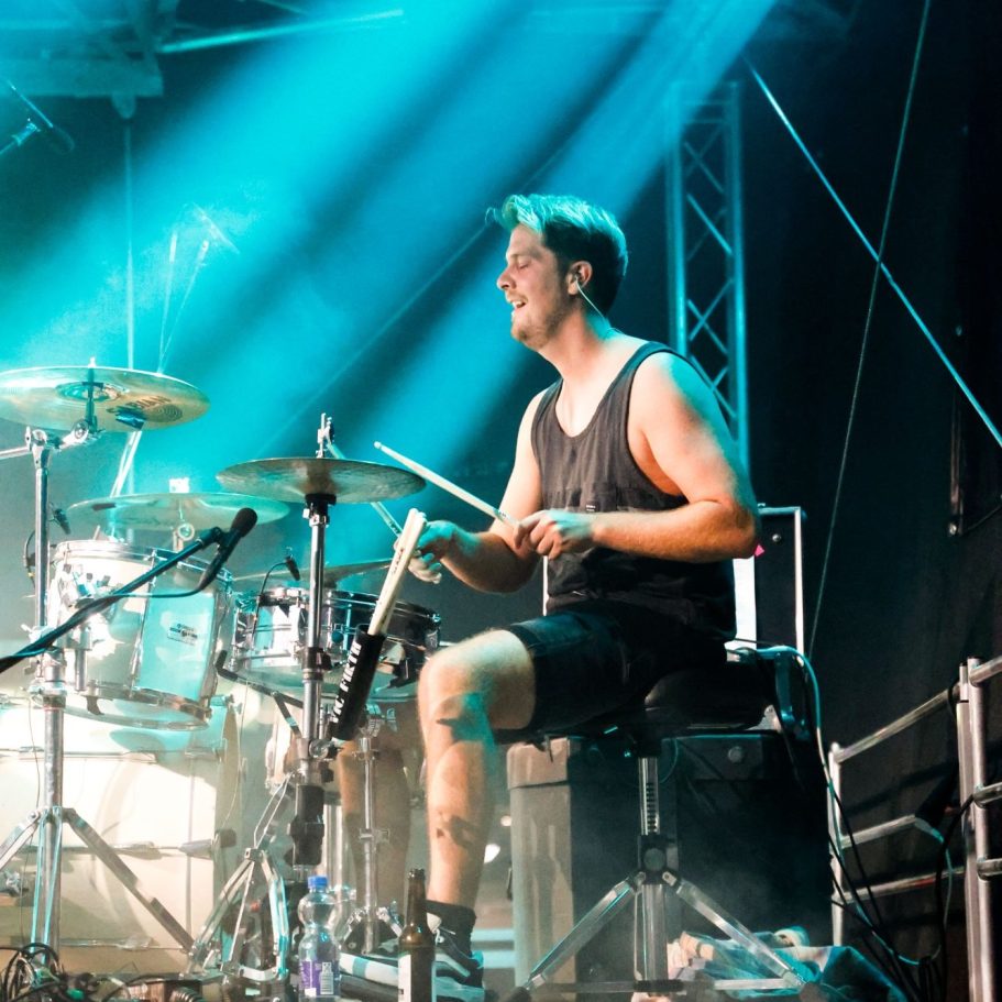 Ein Schlagzeuger spielt energetisch auf der Bühne mit buntem Licht.