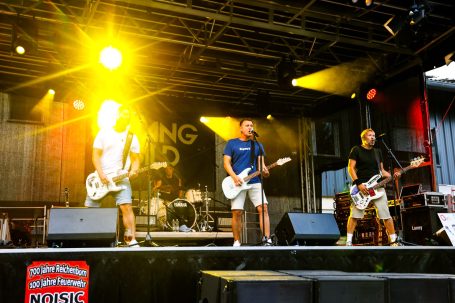 Eine Band spielt live auf einer Bühne mit farbiger Beleuchtung.