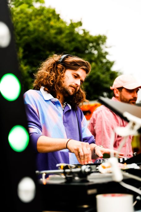 Mann mit lockigem Haar mixt Musik an einem DJ-Setup im Freien.
