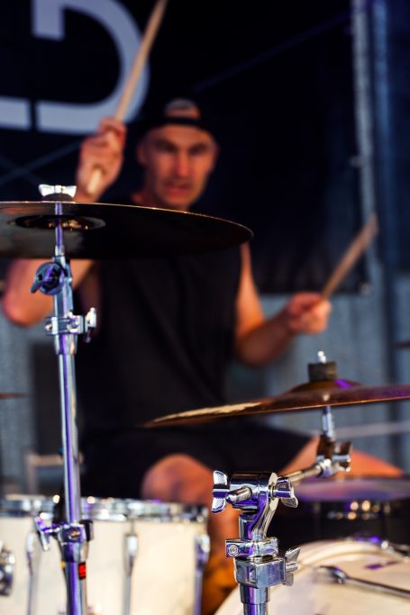 Schlagzeuger in einem schwarzen Tanktop spielt energetisch auf der Bühne.