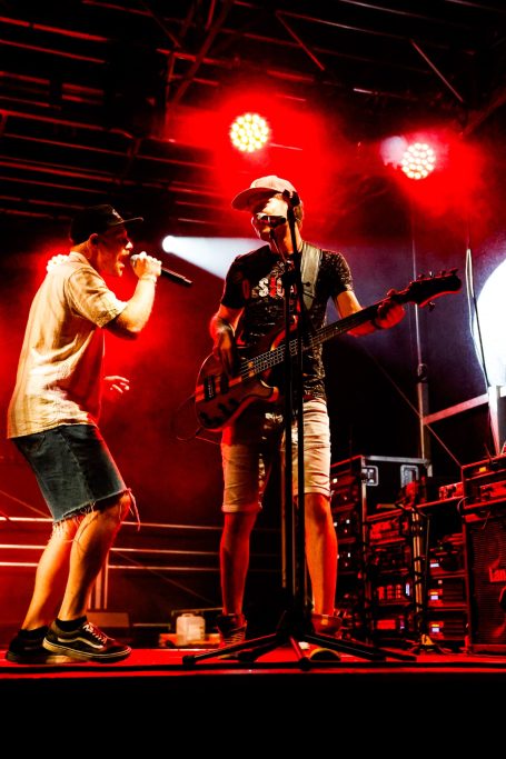 Zwei Musiker auf der Bühne, einer singt ins Mikrofon, der andere spielt E-Gitarre.