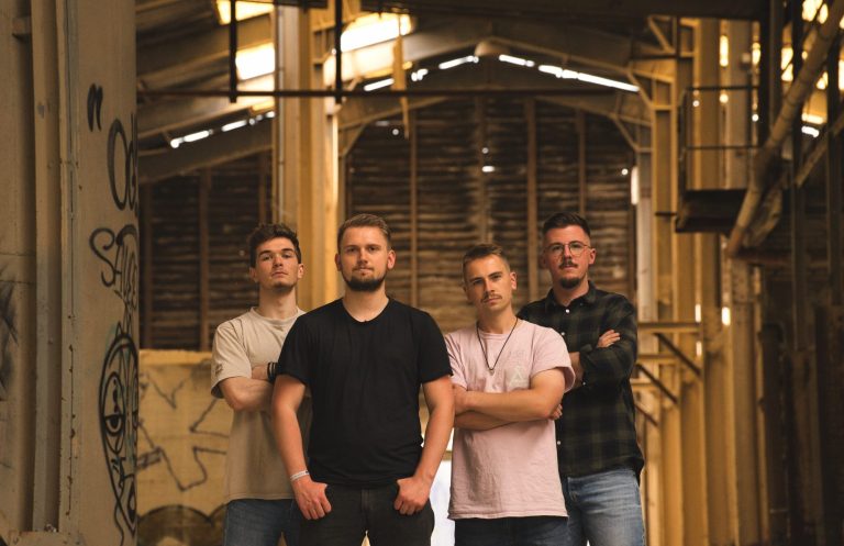 Out Of Plan Band Vier Männer stehen in einer ehemaligen Industrieanlage, mit Graffiti an den Wänden.