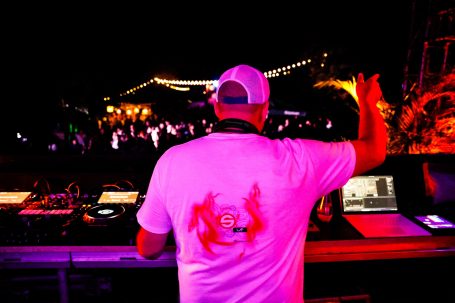 DJ mit Kopfhörern steht vor Publikum und mischt Musik auf einem Festival.