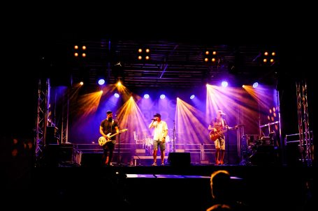 Rockband spielt auf einer Bühne mit bunten Lichtern und einer begeisterten Menge.