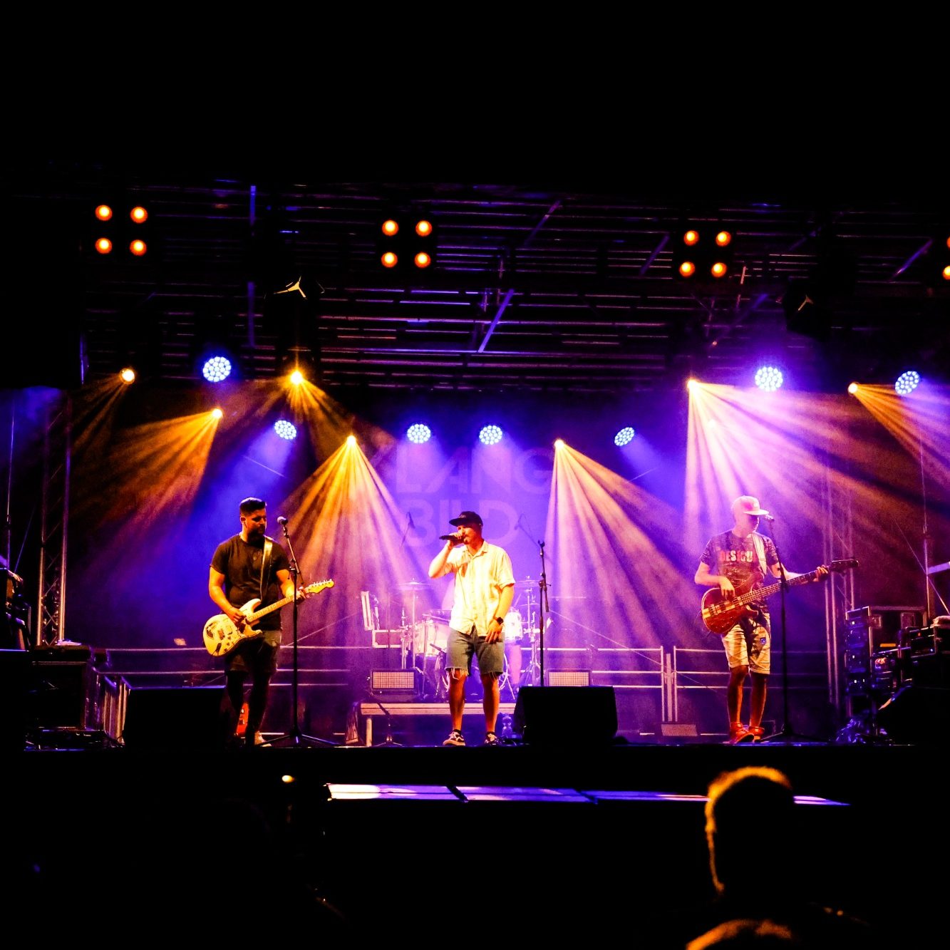 Band auf der Bühne mit bunten Lichtern, Musiker spielen Instrumente.