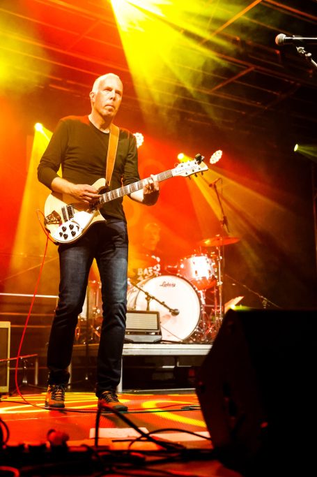 Mann spielt E-Gitarre auf einer Bühne mit bunten Scheinwerfern im Hintergrund.