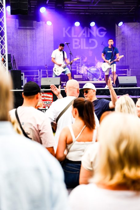 Zwei Musiker auf der Bühne bei einem Konzert, Publikum schaut begeistert zu.