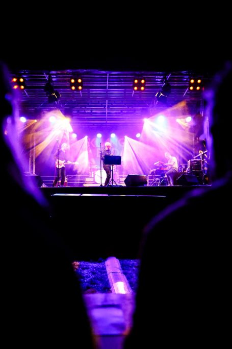 Bühne mit Musiker:innen, buntem Licht und Publikum im Vordergrund.