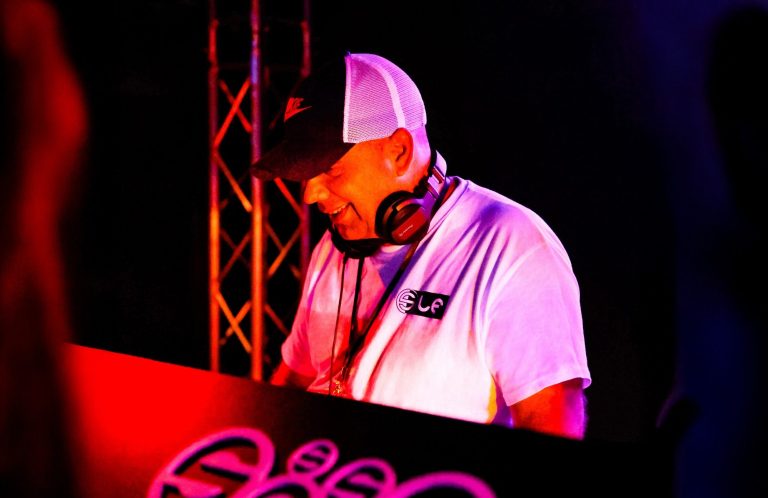 DJ Reifi Pressefoto DJ mit Kopfhörern, Basecap und weißem T-Shirt, fröhlich beim Auflegen.