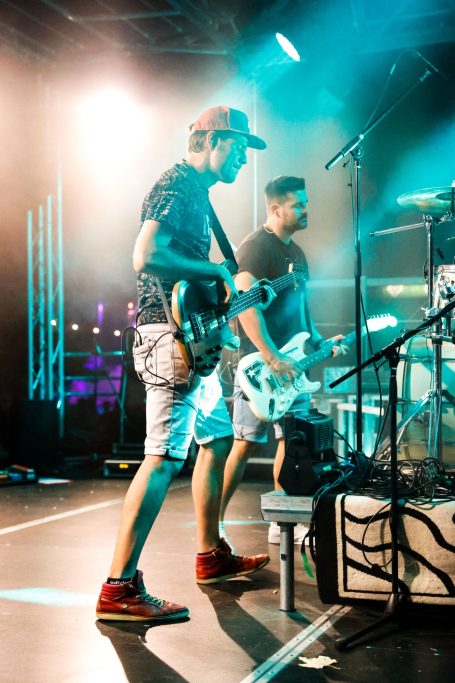 Zwei Musiker auf der Bühne, einer mit Gitarre, der andere mit Bass, in bunten Lichtern.