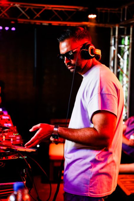 DJ mit Kopfhörern haut Beats auf einem Mischpult in einer neonbeleuchteten Umgebung.