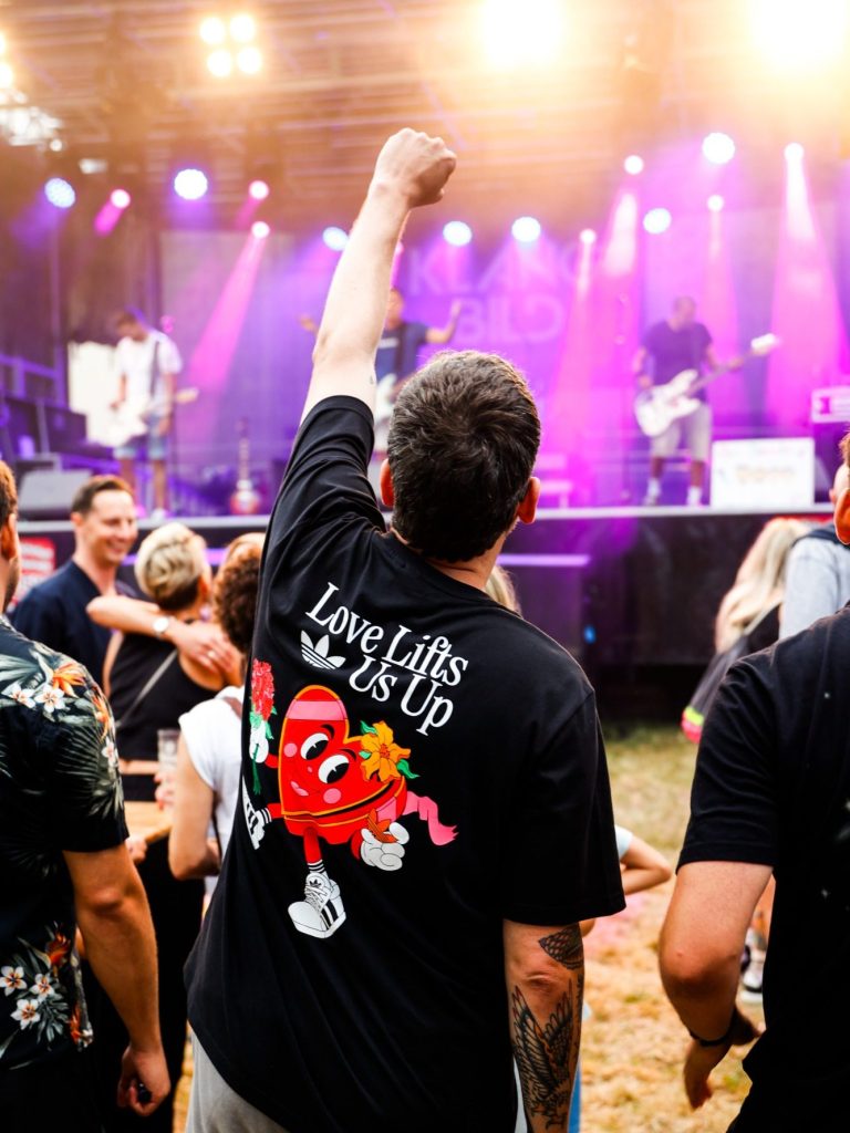Mann mit erhobener Faust und T-Shirt vor einer Bühne bei einem Festival.