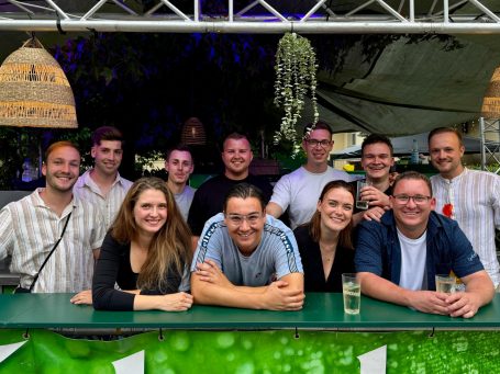 Gruppe von Menschen lächelt hinter einer Bar, mit Getränken in der Hand.