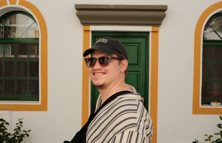 Mann mit Sonnenbrille und gestreiftem Oberteil vor einer grünen Tür.