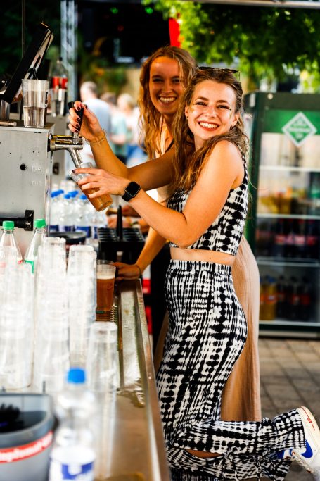 Zwei fröhliche Frauen bedienen an einer Bar mit Getränken.